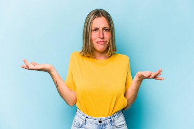 Kafkasyalı genç bir kadın mavi arka planda izole edilmiş sorgulama sırasında omuz silkiyor ve kuşkulanıyor..