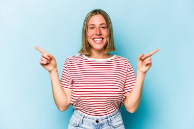 Mavi arka planda izole edilmiş genç beyaz kadın farklı kopya alanlarını gösteriyor, birini seçiyor, parmaklarıyla gösteriyor..