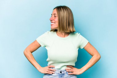 Kafkasyalı genç bir kadın mavi arka planda izole edilmiş. Kendine güvenen, ellerini kalçasında tutan..