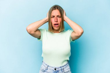 Kafkasyalı genç bir kadın mavi arka planda izole edilmiş kulakları kulaklarıyla kapatıyor çok fazla ses duymamaya çalışıyor..