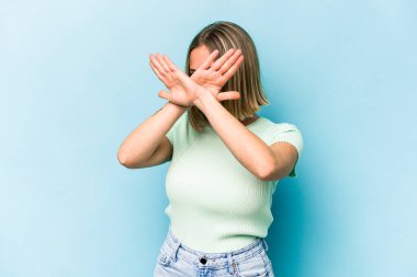 Mavi arka planda izole edilmiş genç beyaz kadın iki kolu çapraz tutuyor, inkar kavramı.