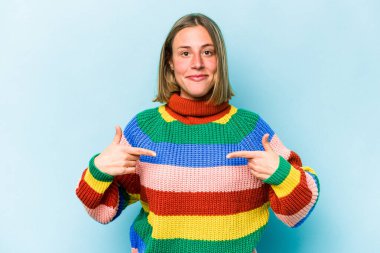 Mavi arka planda izole edilmiş genç beyaz bir kadın gömlek fotokopisini elle gösteriyor, gururlu ve kendinden emin.