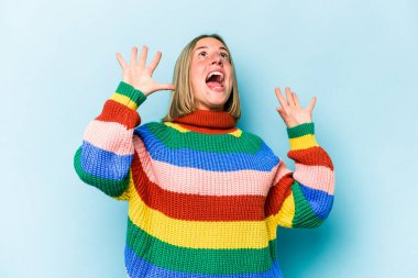 Mavi arka planda izole edilmiş genç beyaz kadın gökyüzüne haykırıyor, yukarı bakıyor, hayal kırıklığına uğramış..