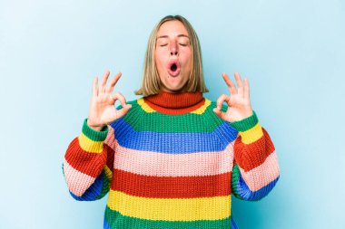 Mavi arka planda izole edilmiş genç beyaz kadın yoğun bir günün ardından rahatlıyor, yoga yapıyor..