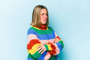 Kafkasyalı genç bir kadın mavi arka planda izole edilmiş şüpheli, belirsiz, seni muayene ediyor..