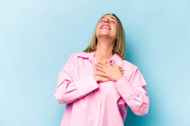 Mavi arka planda soyutlanmış genç beyaz kadın gülüyor, elini yüreğine koyuyor, mutluluk kavramını koruyor..