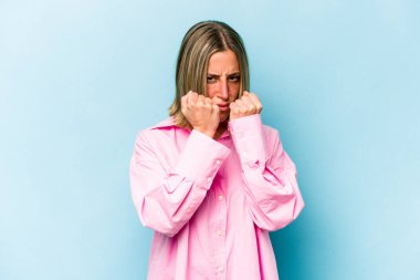 Kafkasyalı genç bir kadın mavi arka planda izole edilmiş bir şekilde bir kavga sonucu yumruk atıyor, öfke ve kavga ediyor, boks yapıyor..