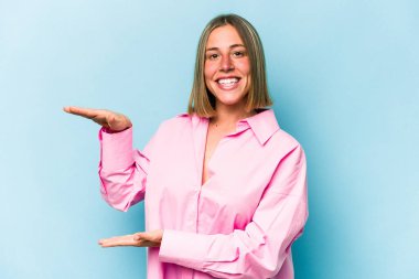 Kafkasyalı genç bir kadın mavi arka planda izole edilmiş. Elinde parmakları olan, gülümseyen ve kendinden emin bir şey var..