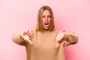 Pembe arka planda izole edilmiş genç beyaz kadın baş parmağını aşağı gösteriyor ve hoşlanmadığını ifade ediyor..
