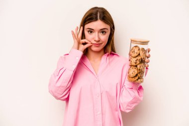 Beyaz arka planda izole edilmiş kurabiye kavanozu tutan beyaz saçlı genç bir kadın. Parmakları dudaklarında bir sır saklıyor..