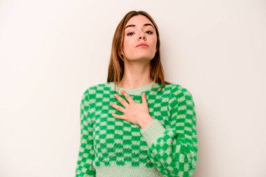 Beyaz arka planda izole edilmiş genç beyaz kadın yemin ediyor, elini göğsüne koyuyor..