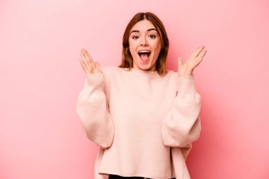 Pembe arka planda izole genç beyaz kadın zaferi ya da başarıyı kutluyor, şaşırıyor ve şok oluyor..