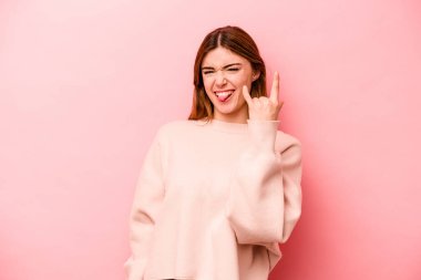 Pembe arka planda izole edilmiş genç beyaz kadın parmaklarıyla taş hareketi gösteriyor.