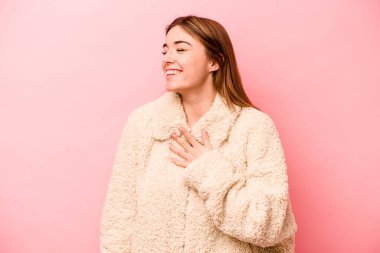 Pembe arka planda soyutlanmış beyaz bir kadın gülüyor, elini yüreğine koyuyor, mutluluk kavramını koruyor..