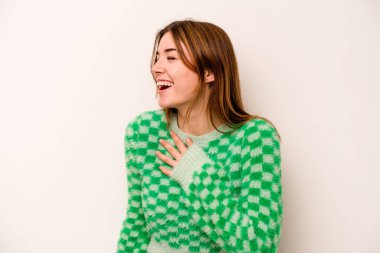 Beyaz arka planda soyutlanmış beyaz tenli genç bir kadın gülüyor, ellerini kalbe koyuyor, mutluluk kavramını koruyor..