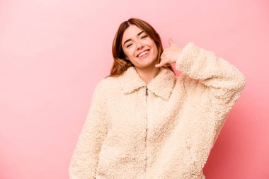 Pembe arka planda izole edilmiş genç beyaz kadın parmaklarıyla bir cep telefonu hareketi gösteriyor..