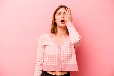 Pembe arka planda izole edilmiş genç beyaz kadın yorgun ve uykulu ellerini başının üstünde tutuyor..