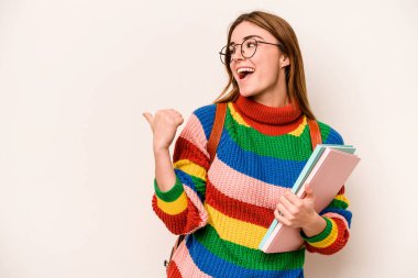 Young student caucasian woman isolated on white background points with thumb finger away, laughing and carefree.