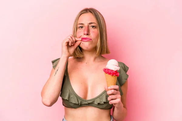 Young caucasian woman wearing a bikini and holding an ice cream isolated on pink background with fingers on lips keeping a secret.