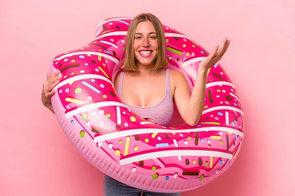 Beyaz bir kadın pembe arka planda izole edilmiş şişme bir yatak tutuyor. Hoş bir sürprizle karşılaşıyor, heyecanlı ve el kaldırıyor..