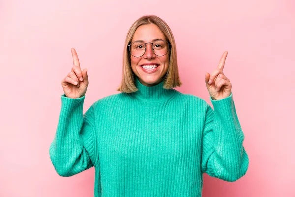 Pembe arka planda izole edilmiş genç beyaz kadın iki parmağı da boş bir alan gösteriyor..