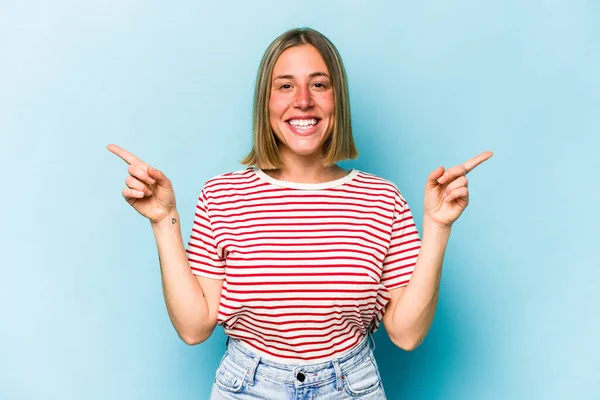 Mavi arka planda izole edilmiş genç beyaz kadın farklı kopya alanlarını gösteriyor, birini seçiyor, parmaklarıyla gösteriyor..
