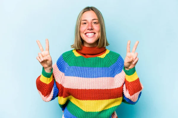 Mavi arka planda izole edilmiş genç beyaz kadın zafer işareti gösteriyor ve gülümsüyor..