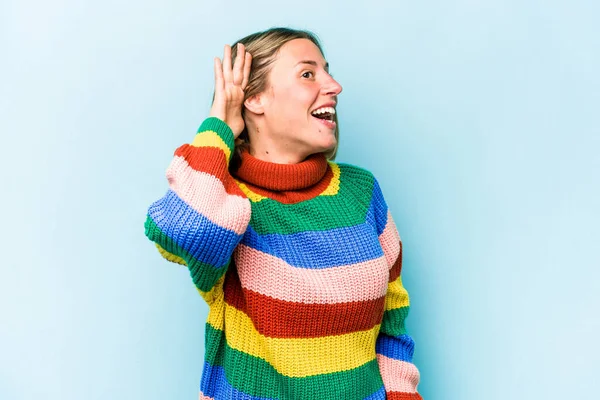 Mavi arka planda izole edilmiş genç beyaz kadın bir dedikoduyu dinlemeye çalışıyor..