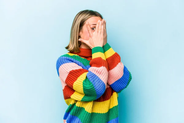 Mavi arka planda izole edilmiş genç beyaz kadın parmaklarıyla gözünü kırp korkmuş ve gergin..