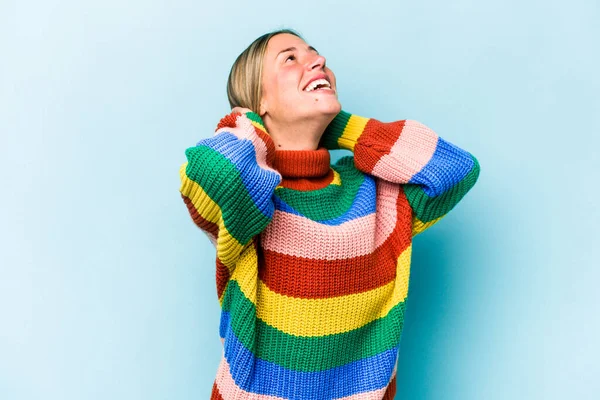 Kafkasyalı genç bir kadın mavi arka planda izole edilmiş, kendinden emin, elleri başının arkasında..