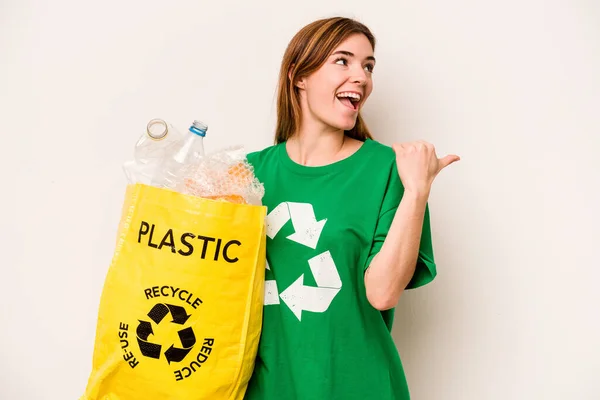 白い背景に親指の指で隔離されたリサイクルするためにビニールボトルでいっぱいの袋を持っている若い女性は笑いと屈託のない — ストック写真