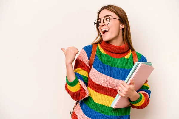 Young student caucasian woman isolated on white background points with thumb finger away, laughing and carefree.