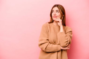 Pembe arka planda soyutlanmış beyaz bir kadın şüpheli ve şüpheci bir ifadeyle yana bakıyor..