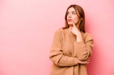 Pembe arka planda soyutlanmış beyaz bir kadın şüpheli ve şüpheci bir ifadeyle yana bakıyor..