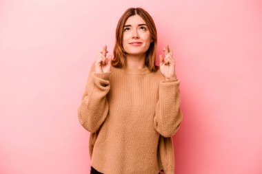 Pembe arka planda izole edilmiş beyaz bir kadın şans getirsin diye dua ediyor.
