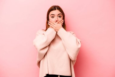 Pembe arka planda izole edilmiş genç, beyaz bir kadın elleri endişeli bir şekilde ağzı örtüyor..