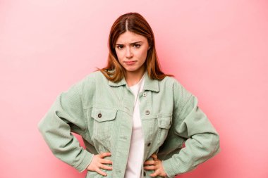Pembe arka planda izole edilmiş genç beyaz kadın kafası karışmış, kuşkulu ve güvensiz hissediyor..