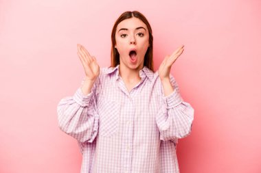 Pembe arka planda izole edilmiş genç beyaz kadın şaşırmış ve şok olmuş..