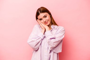 Pembe arka planda izole edilmiş genç beyaz kadın esniyor. Ağzı eliyle kapatan yorgun bir hareket sergiliyor..