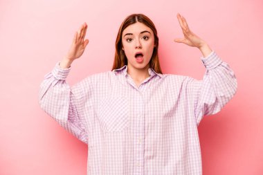 Pembe arka planda izole genç beyaz kadın zaferi ya da başarıyı kutluyor, şaşırıyor ve şok oluyor..