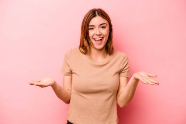 Pembe arka planda izole edilmiş genç beyaz kadın kollarıyla ölçek oluşturuyor, mutlu ve kendinden emin hissediyor..