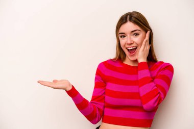 Beyaz arka planda izole edilmiş genç beyaz kadın avuç içinde fotokopi alanı tutuyor, el üstünde tutuyor. Şaşırmış ve mutlu..