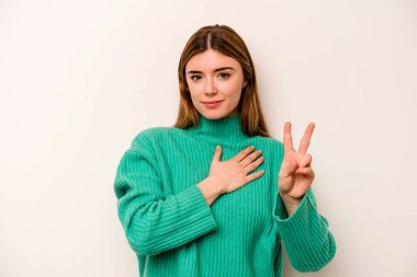 Beyaz arka planda izole edilmiş genç beyaz kadın yemin ediyor, elini göğsüne koyuyor..