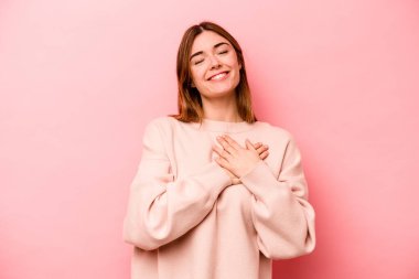 Pembe arka planda soyutlanmış beyaz bir kadın gülüyor, elini yüreğine koyuyor, mutluluk kavramını koruyor..