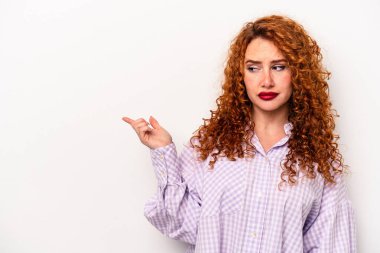 Beyaz arka planda soyutlanmış beyaz tenli genç bir kadın gülümsüyor ve boş alanda bir şeyler gösteriyor..