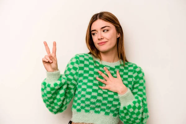 Beyaz arka planda izole edilmiş genç beyaz kadın yemin ediyor, elini göğsüne koyuyor..