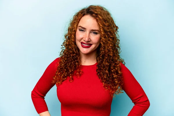 Genç, beyaz, mavi arka planda izole edilmiş, elleri kalçasında tutan, kendine güvenen bir kadın..