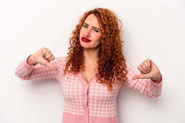 Beyaz arka planda izole edilmiş genç kızıl saçlı kadın baş parmağını aşağı gösteriyor, hayal kırıklığı konsepti..