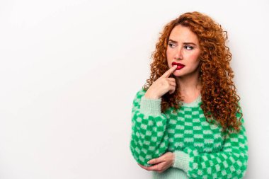 Beyaz arka planda soyutlanmış beyaz tenli genç bir kadın şüpheli ve şüpheci bir ifadeyle yana bakıyor..