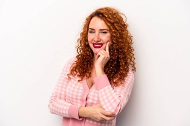 Beyaz arka planda soyutlanmış beyaz tenli genç bir kadın gülümsüyor ve kendinden emin, elleriyle çenesine dokunuyor..